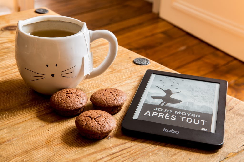 A cozy scene with tea, muffins, and an e-reader on a wooden table.