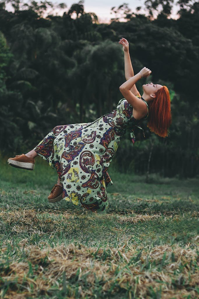 A woman in a vibrant dress appears to levitate in a lush outdoor setting, surrounded by greenery.